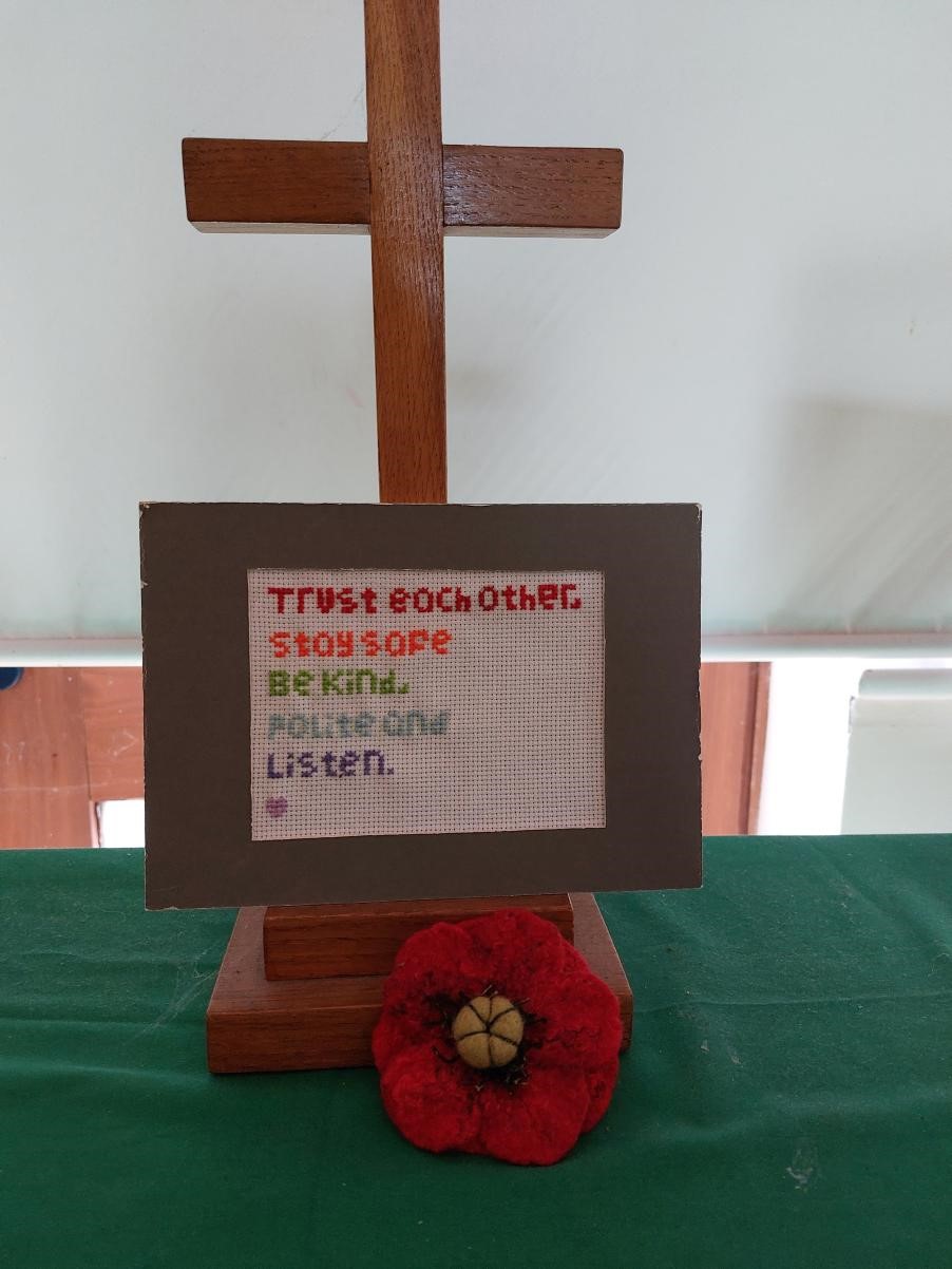 A cross with values on a cross stitched plaque with a felt poppy